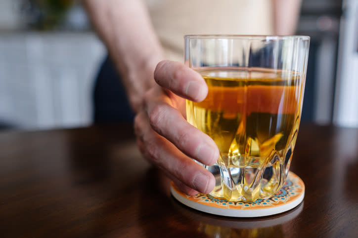 A person’s hand holding a glass of tea on a decorative coaster, set on a wooden table