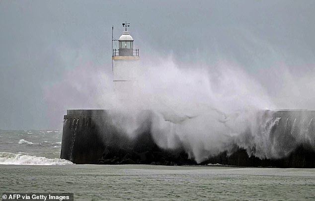 Waves crash over Newhaven Lighthouse in East Sussex today amid the stormy weather