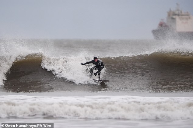 A surfer catches a wave in the wind at Tynemouth Longsands in North Tyneside today