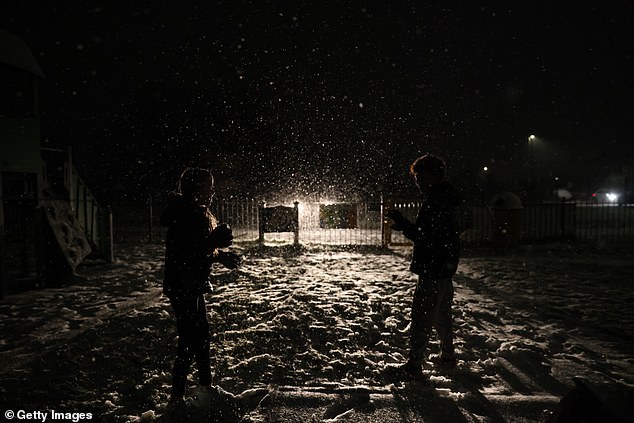 Children play in the snow as their father keeps watch from his car