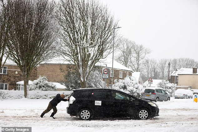 A person helps push a stranded car stuck in snow in Bradford today