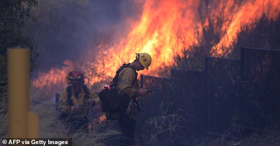 Firefighters work to put out a brush fire burning near homes in Pacific Palisades, California, on January 7, 2025. A fast-moving brushfire in a Los Angeles suburb burned buildings and sparked evacuations Tuesday as "life threatening" winds whipped the region. More than 200 acres (80 hectares) was burning in Pacific Palisades, a upscale spot with multi-million dollar homes in the Santa Monica Mountains, shuttering a key highway and blanketing the area with thick smoke. (Photo by David Swanson / AFP) (Photo by DAVID SWANSON/AFP via Getty Images)