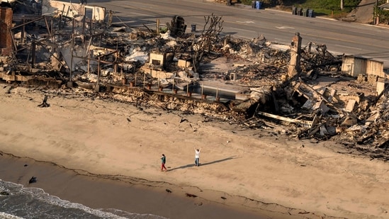 In this aerial view taken from a helicopter, a man waves on the beach in front of burned homes during the Palisades fire in the Malibu, Los Angeles county, (AFP)