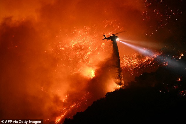 A fire fighting helicopter drops water as the Palisades fire grows