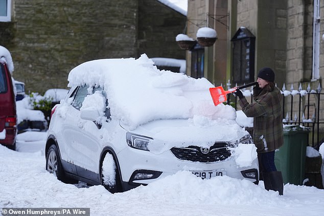 A driver clears snow from a car in Allendale, Northumberland, today amid the severe weather