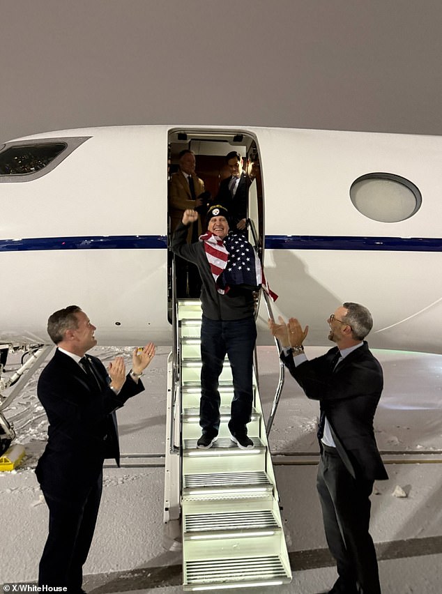 Marc Fogel (center), drapped in an American flag, returns to U.S. soil for the first time since 2021. National Security Adviser Mike Waltz (L) and United States Envoy for Hostages Adam Boehler (R) can be seen applauding his arrival