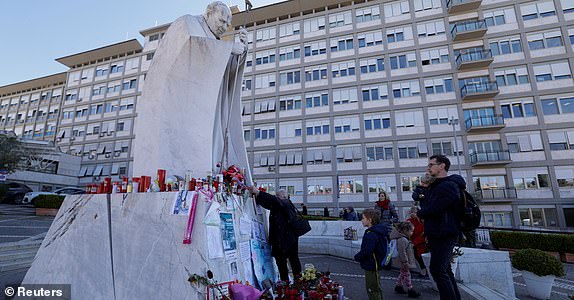 People pray near the statue of late Pope John Paul II outside Gemelli Hospital where Pope Francis is admitted for treatment, in Rome, Italy, March 5, 2025. REUTERS/Remo Casilli