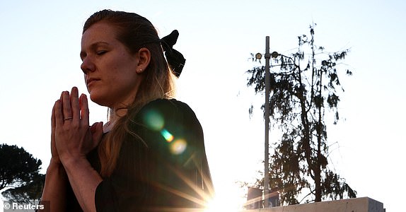 A woman prays near the statue of late Pope John Paul II outside Gemelli Hospital, where Pope Francis is admitted for treatment, in Rome, Italy, March 4, 2025. REUTERS/Guglielmo Mangiapane