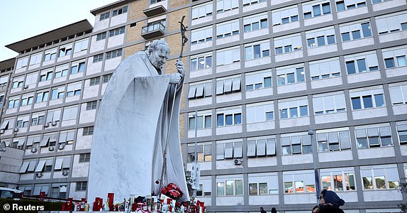 A person stands next to the statue of late Pope John Paul II outside Gemelli Hospital, where Pope Francis is admitted for treatment, in Rome, Italy, March 4, 2025. REUTERS/Yara Nardi