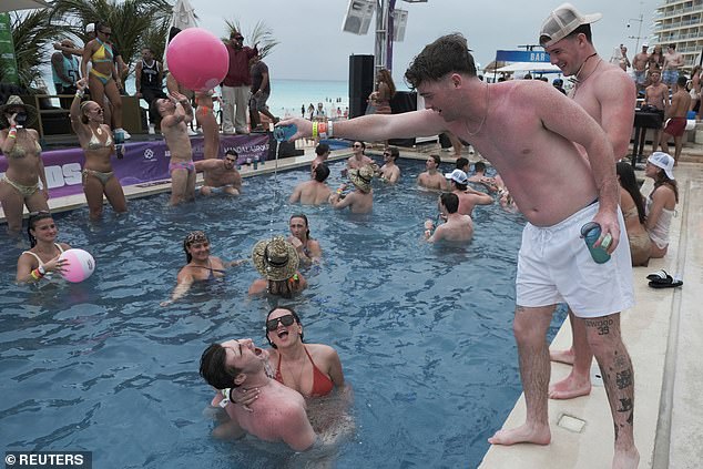 A man pours alcohol into another man's mouth as they party in a pool in Cancun