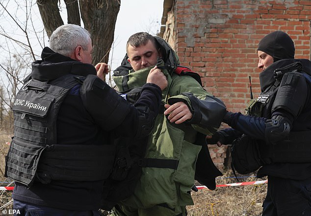 Ukrainian sappers help dress a comrade in a heavy armored suit during demining operations in the Kharkiv area, northeastern Ukraine, 12 March 2025