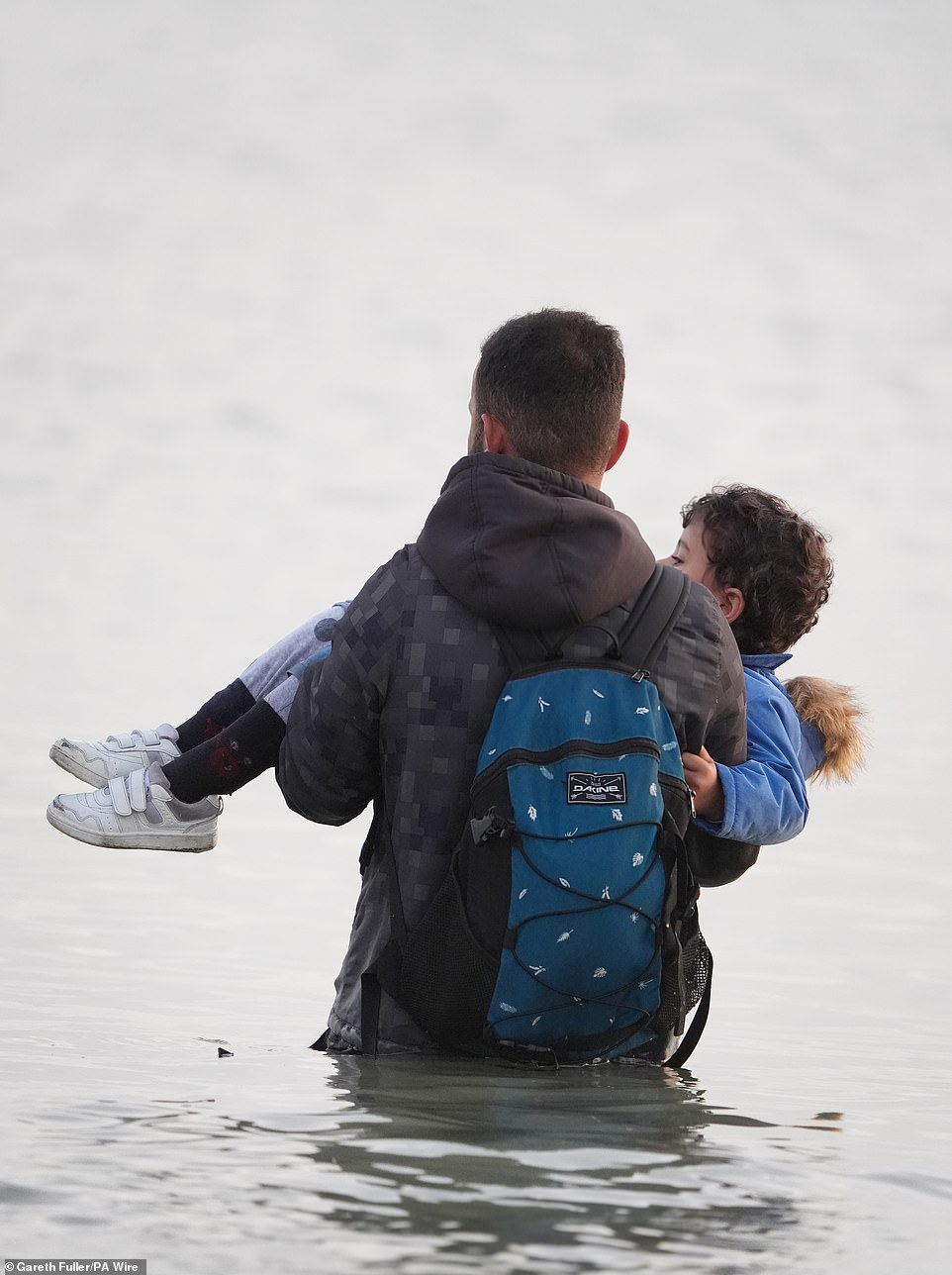 A man carries a young child to a small boat off the coast of France in a bid to reach the UK by crossing the Channel