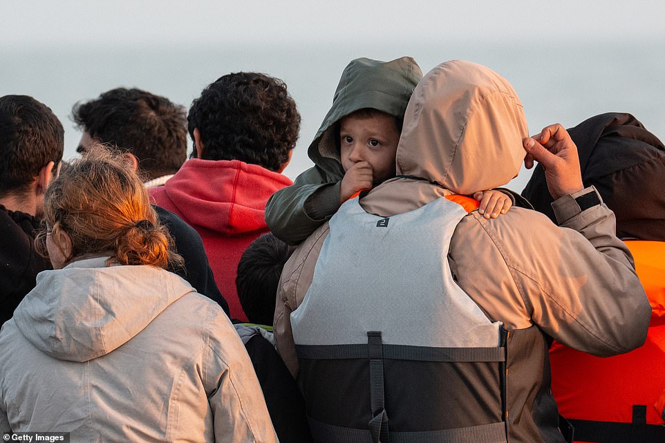 A young boy appears nervous as he is held on a small boat transporting refugees and migrants to the UK