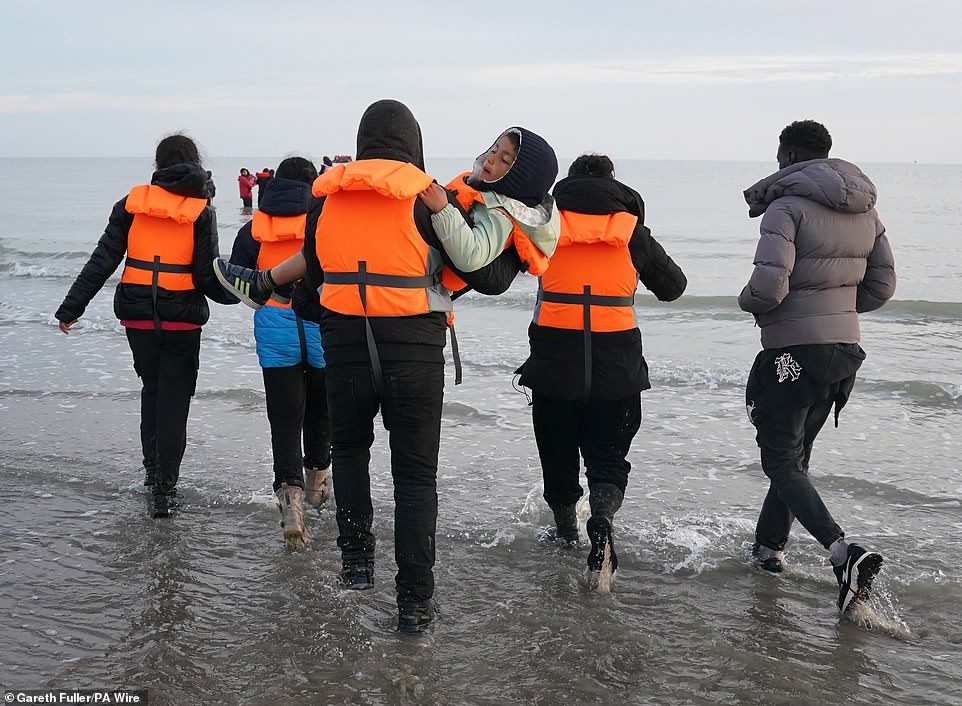 A group of people thought to be migrants walk towards the sea to board a small boat leaving the beach at Gravelines, France