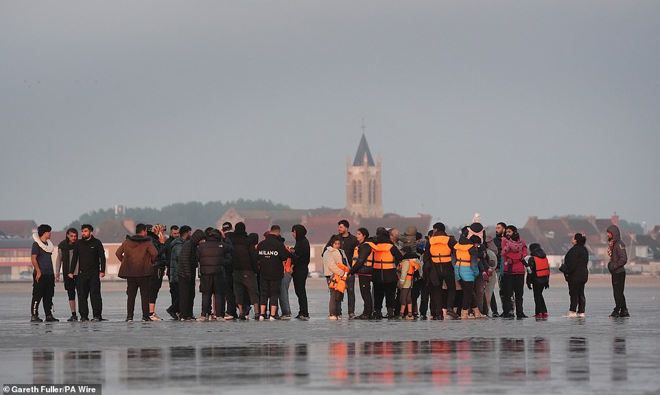 A group of people including women and young children are seen waiting to try and catch a boat to the UK