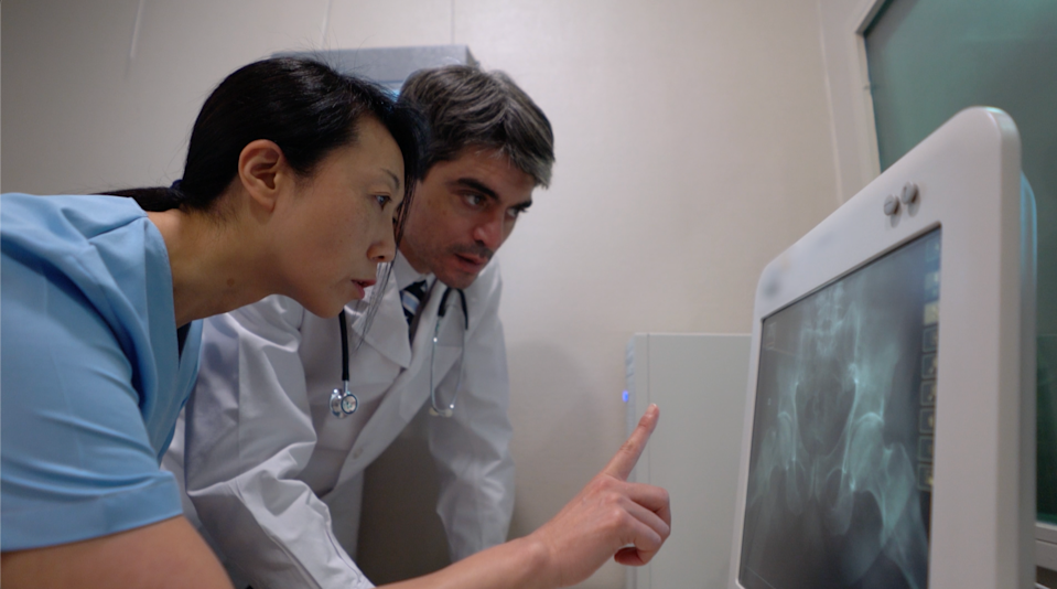 Two medical professionals examine an X-ray on a computer monitor, discussing potential diagnoses