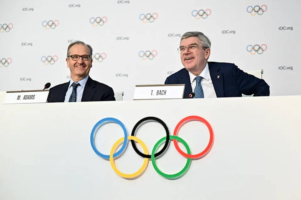 Outgoing International Olympic Committee (IOC) President Thomas Bach (R) smiles next to IOC spokesman Mark Adams during a closing press conference during the 144th IOC Session in Costa Navarino, Greece, on March 21, 2025. (Photo by Fabrice COFFRINI / AFP) (Photo by FABRICE COFFRINI/AFP via Getty Images)