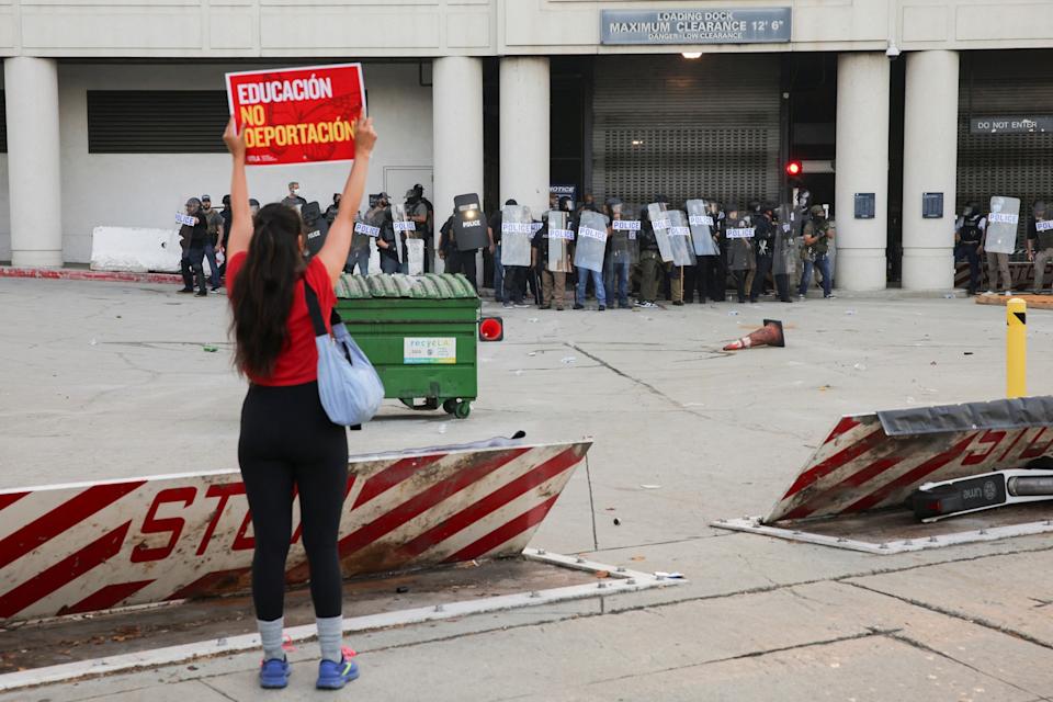 Daniel Cole/Reuters - PHOTO: A demonstrator holds a placard infront of the police as protesters gather around the Los Angeles Federal Building following multiple detentions by Immigration and Customs Enforcement (ICE), in downtown Los Angeles, June 6, 2025.