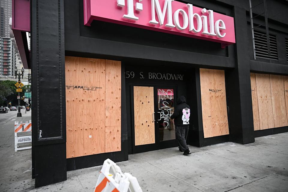 A man walks past a boarded up T-Mobile store that was looted overnight on Sunday (AFP/Getty)