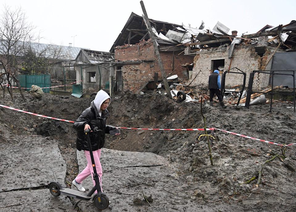 A girl carries a kick scooter as she walks past a crater after a missile strike in a village, near the western Ukrainian city of Lviv,