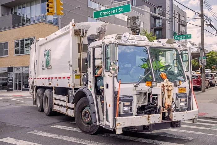 Garbage truck turning at a city intersection with visible street signs.