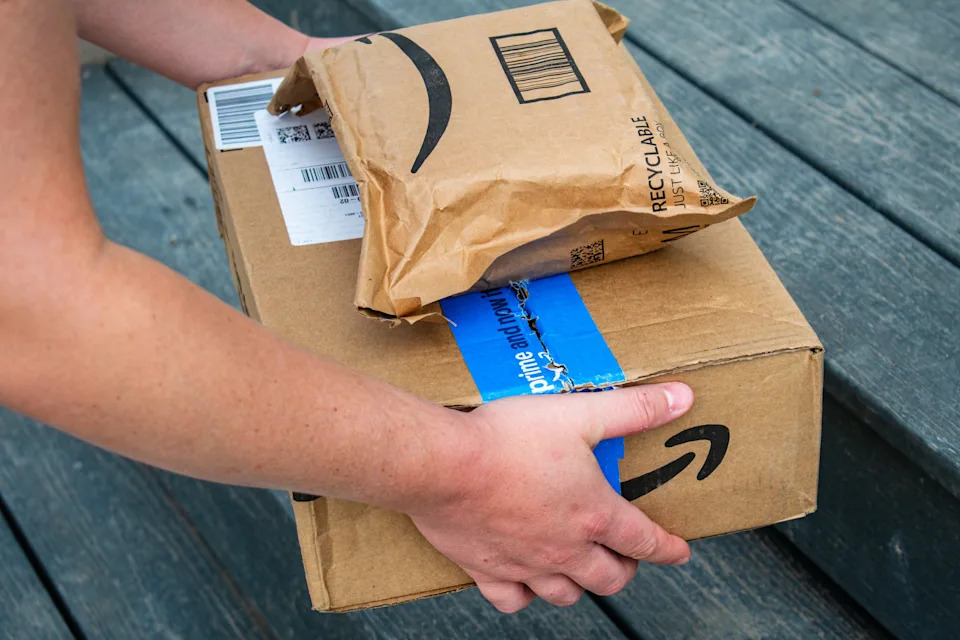 Person holding two Amazon packages on a wooden deck.