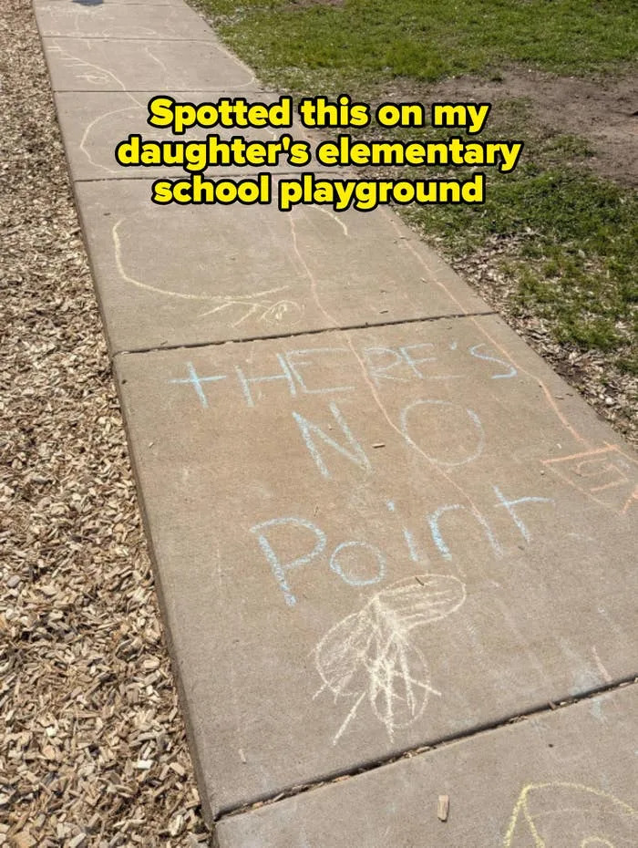 Chalk drawing on a sidewalk reads "THERE'S NO Point" with abstract shapes and doodles nearby. Caption: "Spotted this on my daughter's elementary school playground"