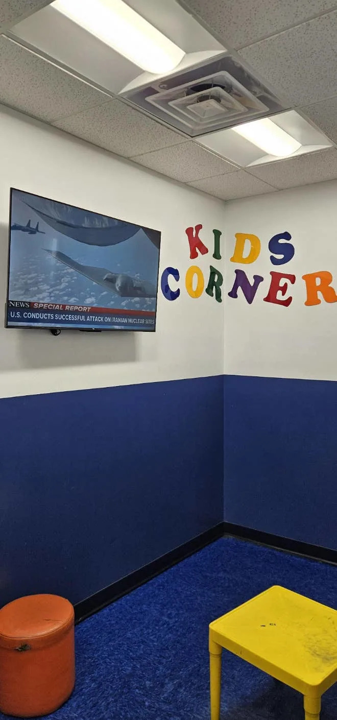 Room corner with a “Kids Corner” sign and TV displaying news of a successful attack on an Iranian nuclear site