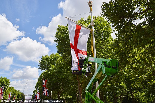 St George's flags are hoisted onto flagpoles on The Mall ahead of the open-top bus parade at lunchtime