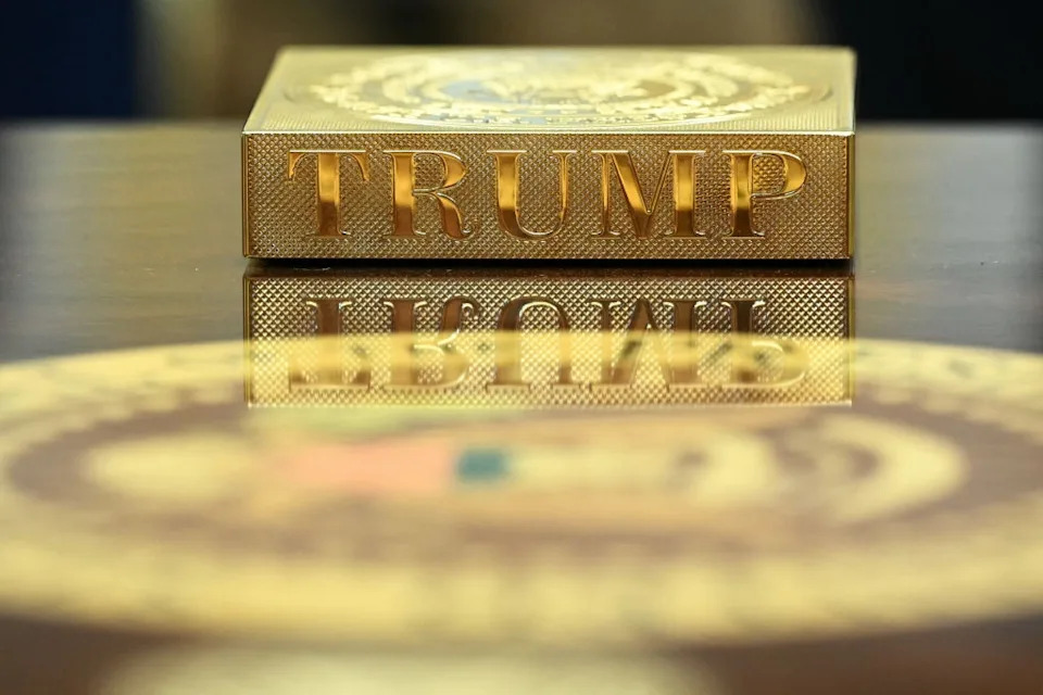 Gold-plated box with the word "TRUMP" engraved, reflected on a shiny surface with part of a United States seal visible in the foreground