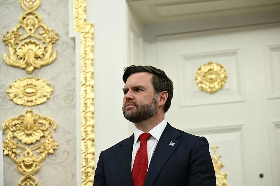 Man in formal suit with red tie standing in an ornate room with golden accents