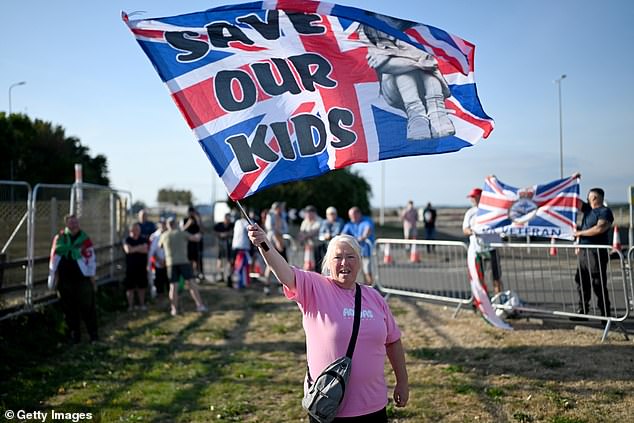 A woman waves a Union Jack flag with the description 'Save our kids' during a protest about illegal immigration outside a Holiday Inn in Rhoose, Wales