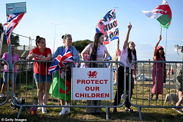 Protestors with a sign stating 'Protect our children' gather outside a Holiday Inn on August 22, 2025 in Rhoose, Wales