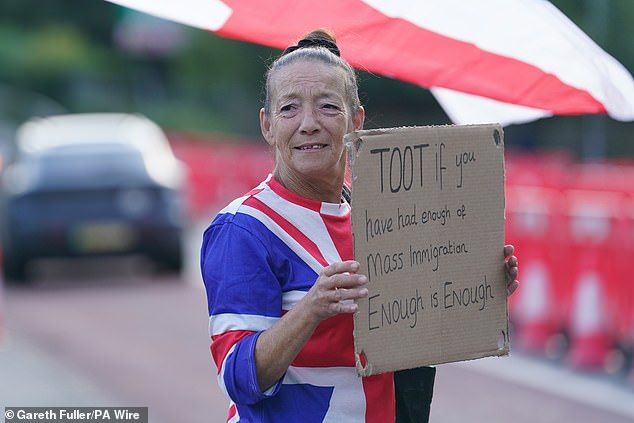 A woman taking part in an anti-migrant protest in Ashford holds a sign saying 'TOOT if you have had enough of mass immigration, Enough is Enough'
