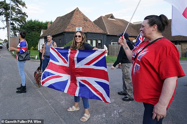 A woman holds a Union Jack while taking part in a protest outside a Holiday Inn in Ashford, Kent, believed to be housing asylum seekers