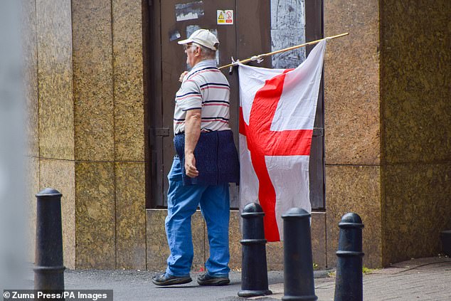 Pictured: an anti-migrant protestor walks with a flag outside of Britannia Hotel on August 23. The hotel, which is being used to accommodate hundreds of migrants, has often become the centre of focus for a group of female anti-migrant protesters dubbed the 'Pink Ladies'