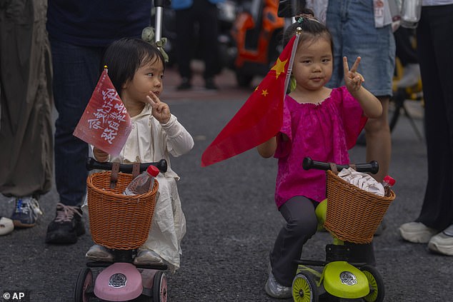 Two girls hold flags as they show the victory sign while waiting to watch military parade to commemorate the 80th anniversary of the end of World War II in Beijing