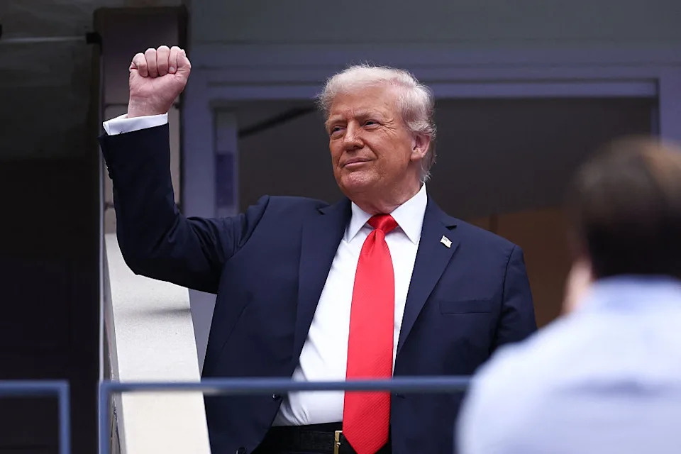 Person in a suit with a red tie raises a fist confidently in an outdoor setting