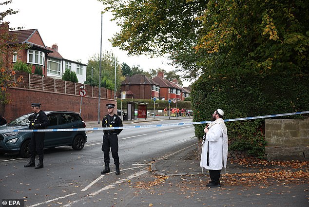 A member of the a Jewish Community holds a Torah at a police cordon in Manchester today