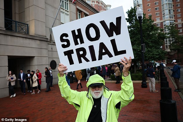 ALEXANDRIA, VIRGINIA - OCTOBER 08: Activist Bill Christeson holds up a sign that reads "Show Trial" outside the U.S. District Court for the Eastern District of Virginia's Bryan Courthouse ahead of the arraignment of former FBI Director James Comey on October 08, 2025 in Alexandria, Virginia. Comey will be arraigned today after being indicted by a Virginia grand jury on charges of making a false statement and obstruction during congressional testimony in 2020. (Photo by Win McNamee/Getty Images)