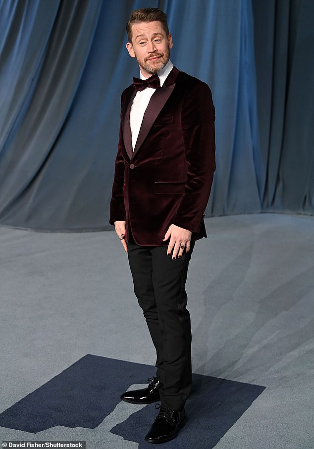 Macaulay Culkin dressed for the occasion wearing a pair of black slacks as well as a dark red velvet blazer and bowtie