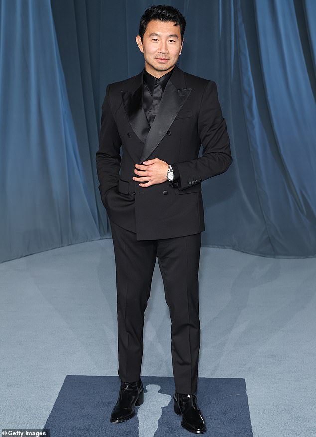 Simu Liu stopped for a photo session at the venue in a double-breasted black suit and also donned a black shirt underneath