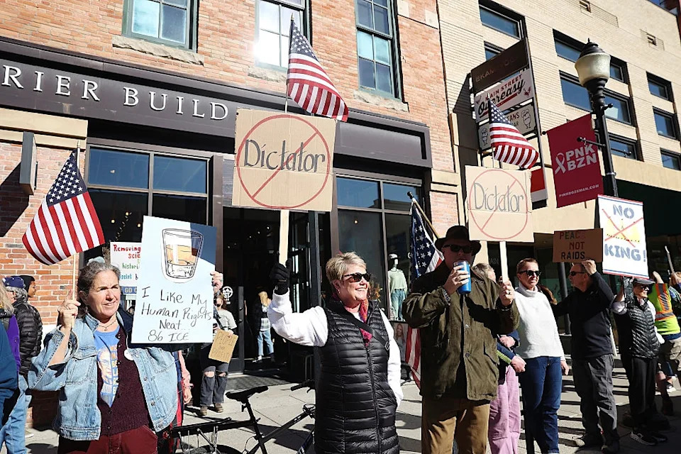 Protesters outside a building hold signs against dictatorship; some wave U.S. flags. One sign says, "I like my human rights and Big Tec."