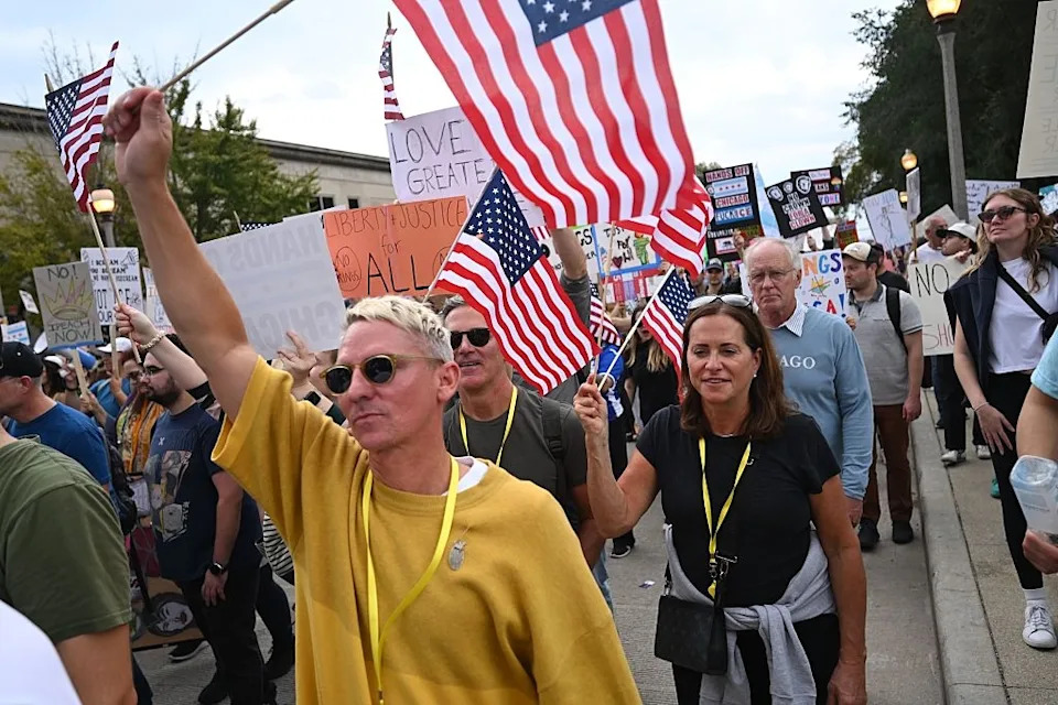 People at a protest holding signs and American flags, engaging in advocacy or demonstration on a city street