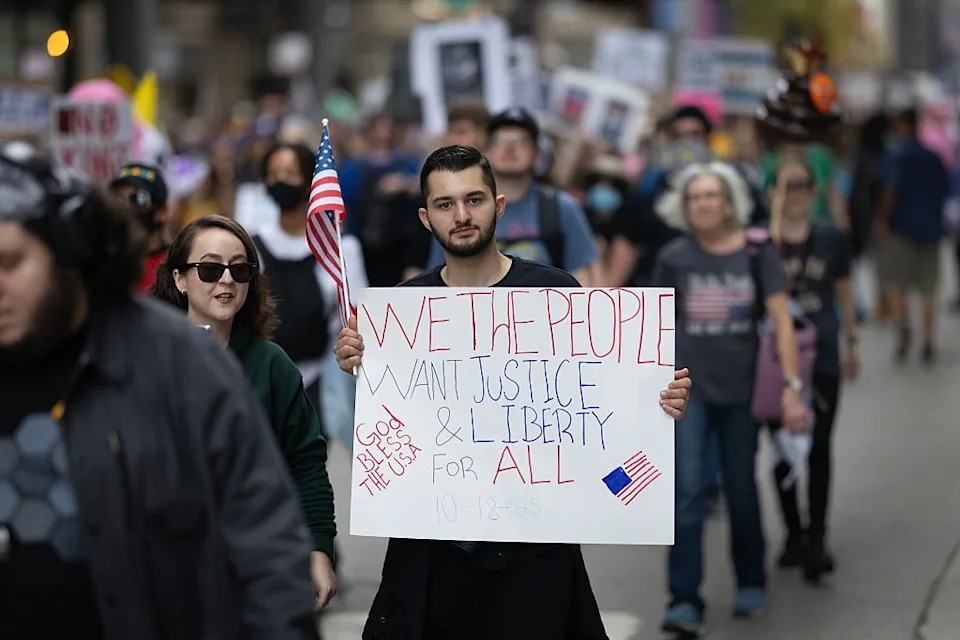 Person holds a sign reading "We the People Want Justice & Liberty for All" during a protest march, surrounded by a crowd of demonstrators