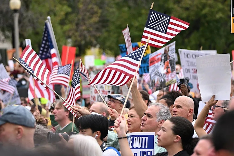 People holding American flags and protest signs at a public demonstration, conveying a sense of activism and unity