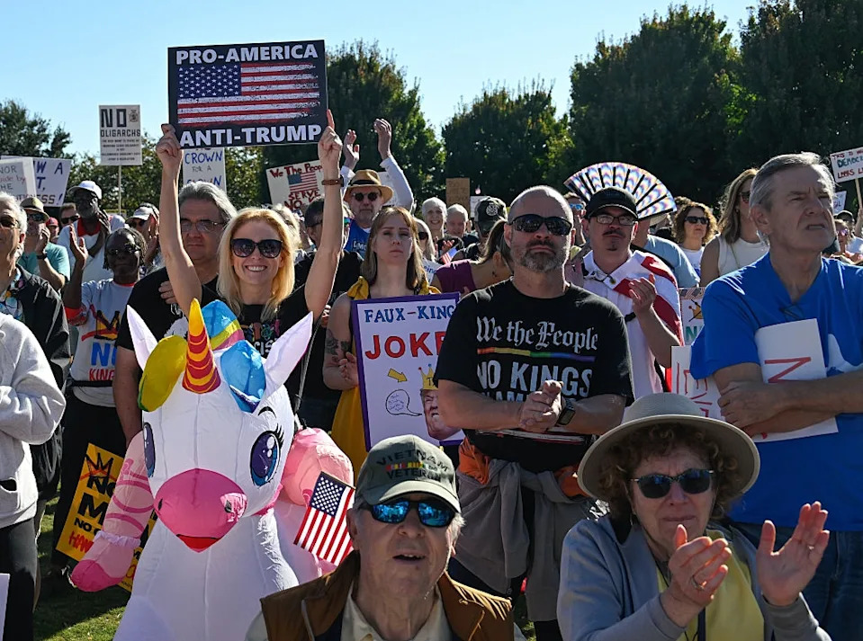 People at a rally holding signs with various messages, including "Pro-America Anti-Trump," and carrying an inflatable unicorn