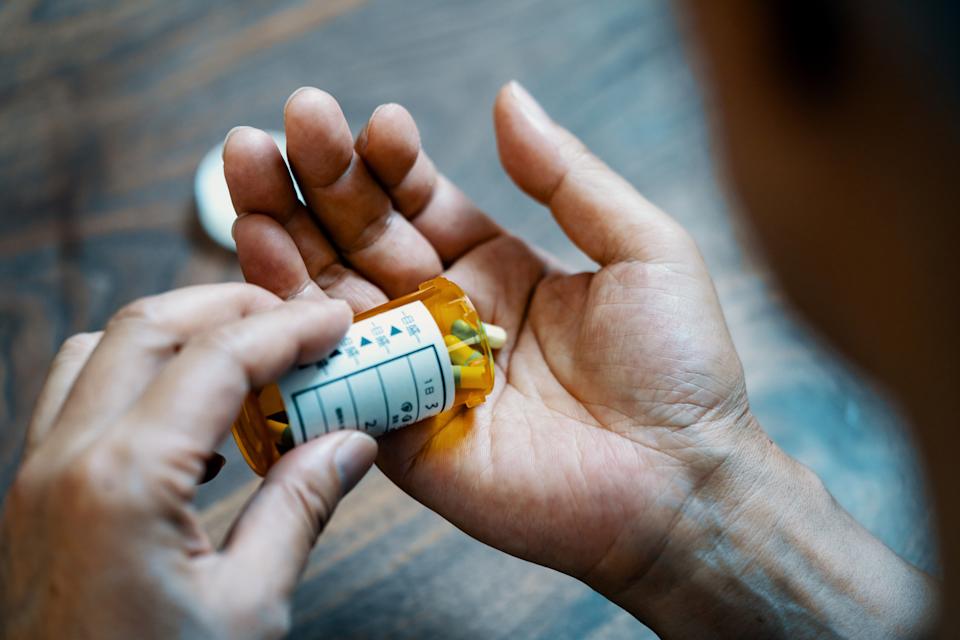 A hand pours pills from a prescription bottle into the other hand over a table surface