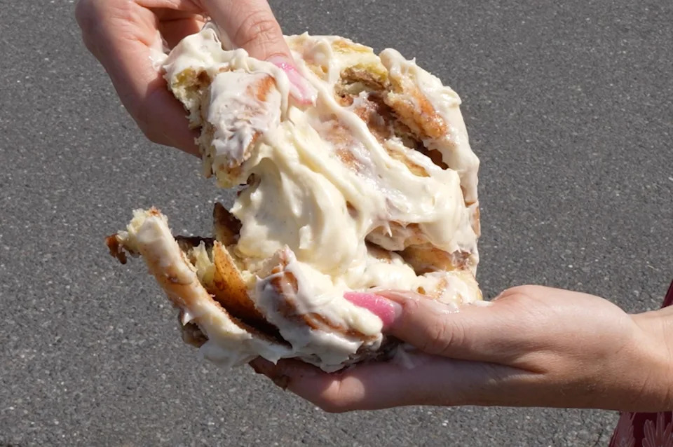 Cinnamon bun covered in icing being pulled apart