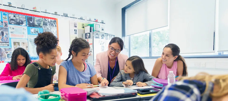 Teacher assisting a diverse group of engaged students with classwork at a bright, modern classroom desk